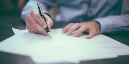 A man in business attire is using a pen to complete some paperwork