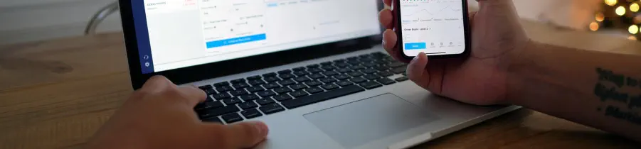 A person is looking at an open laptop and also at their cell phone